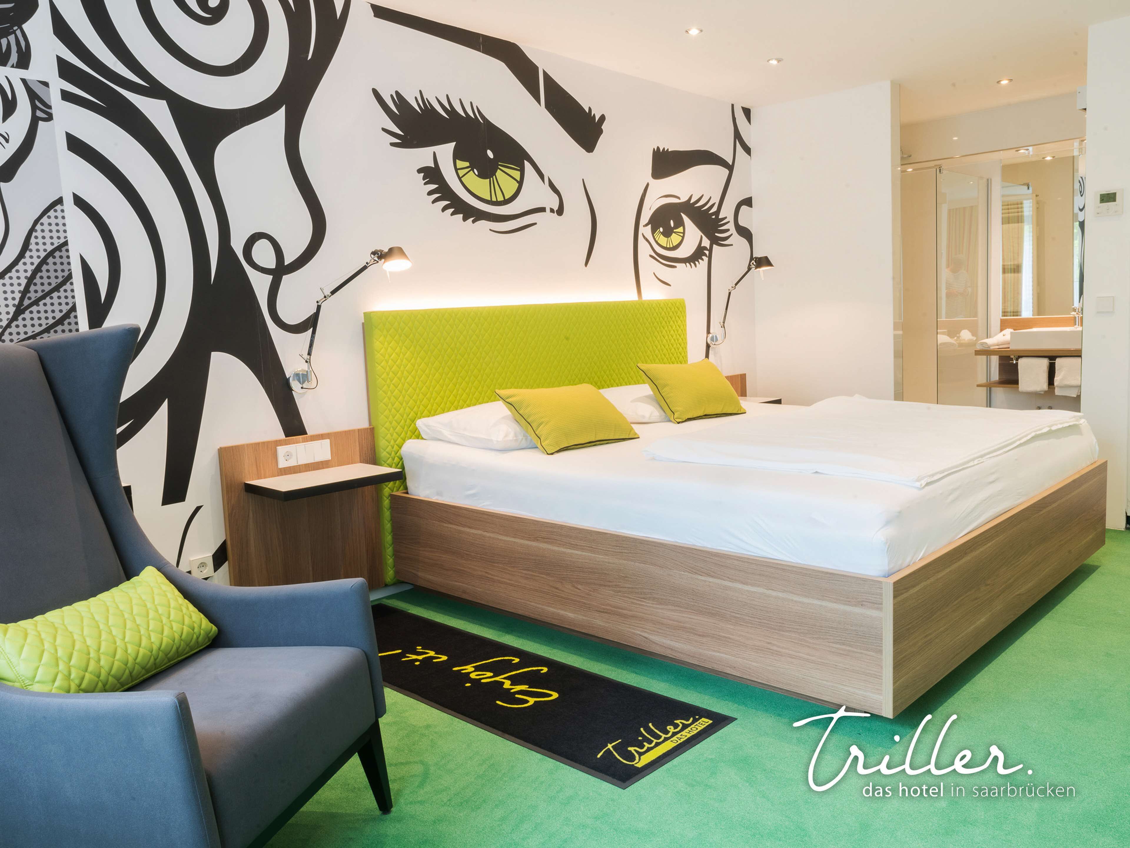 A modern hotel room with a large bed, a bedside table, a chair, and a wall with a large abstract design.