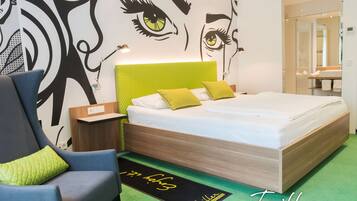 A modern hotel room with a large bed, a bedside table, a chair, and a wall with a large abstract design.