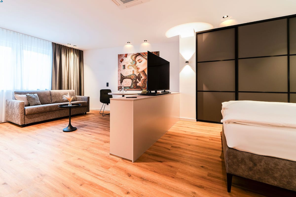 A modern hotel room with a sofa, a small table, a desk with a flat-screen TV, and a bed.