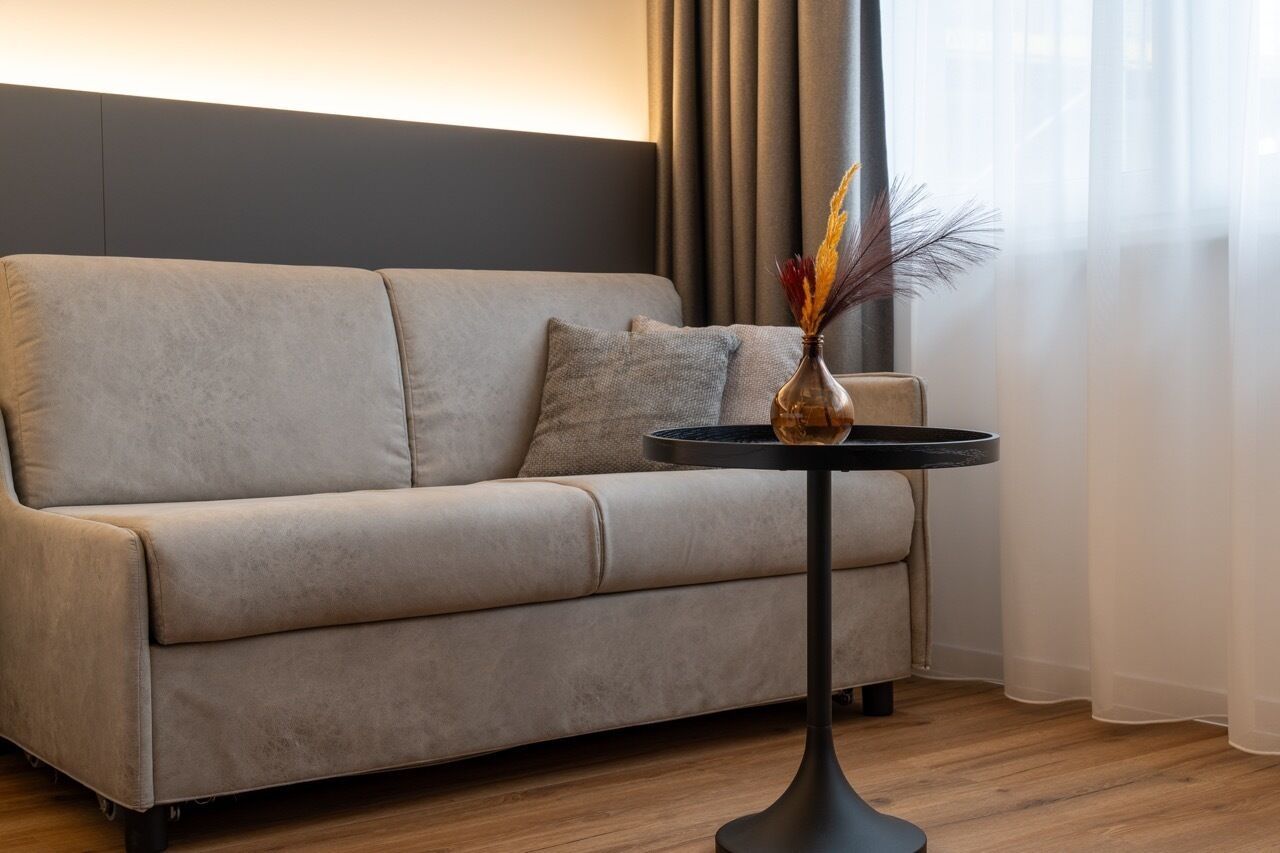 A modern living room with a beige sofa, a round black table, and a vase with dried plants.