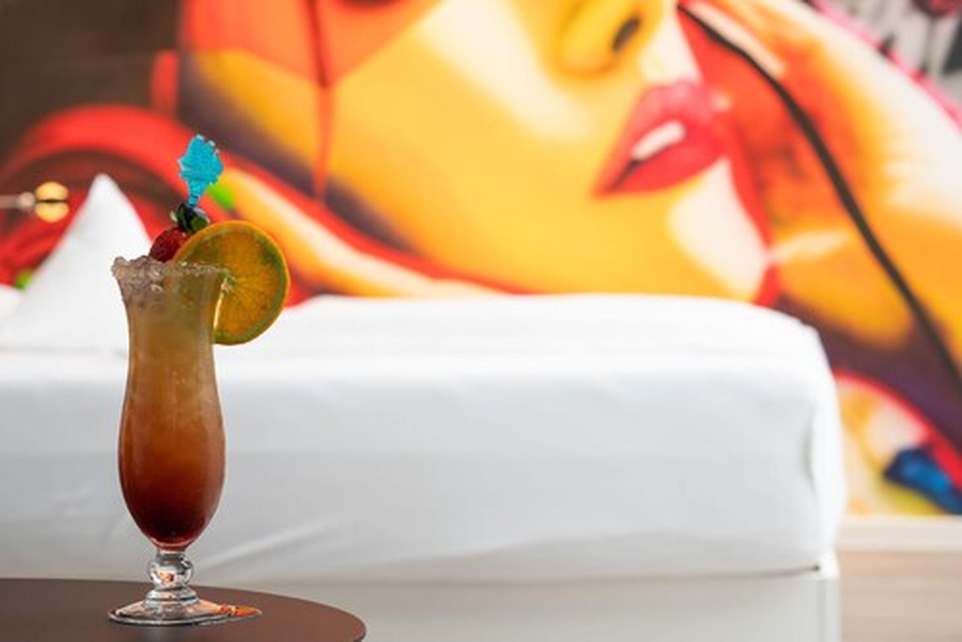 A cocktail in a tall glass with a slice of orange and a blue garnish on a table.