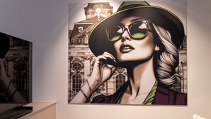 A wall with a large framed artwork depicting a person in a hat and glasses. - Hotel Am Triller (Saarbrücken)