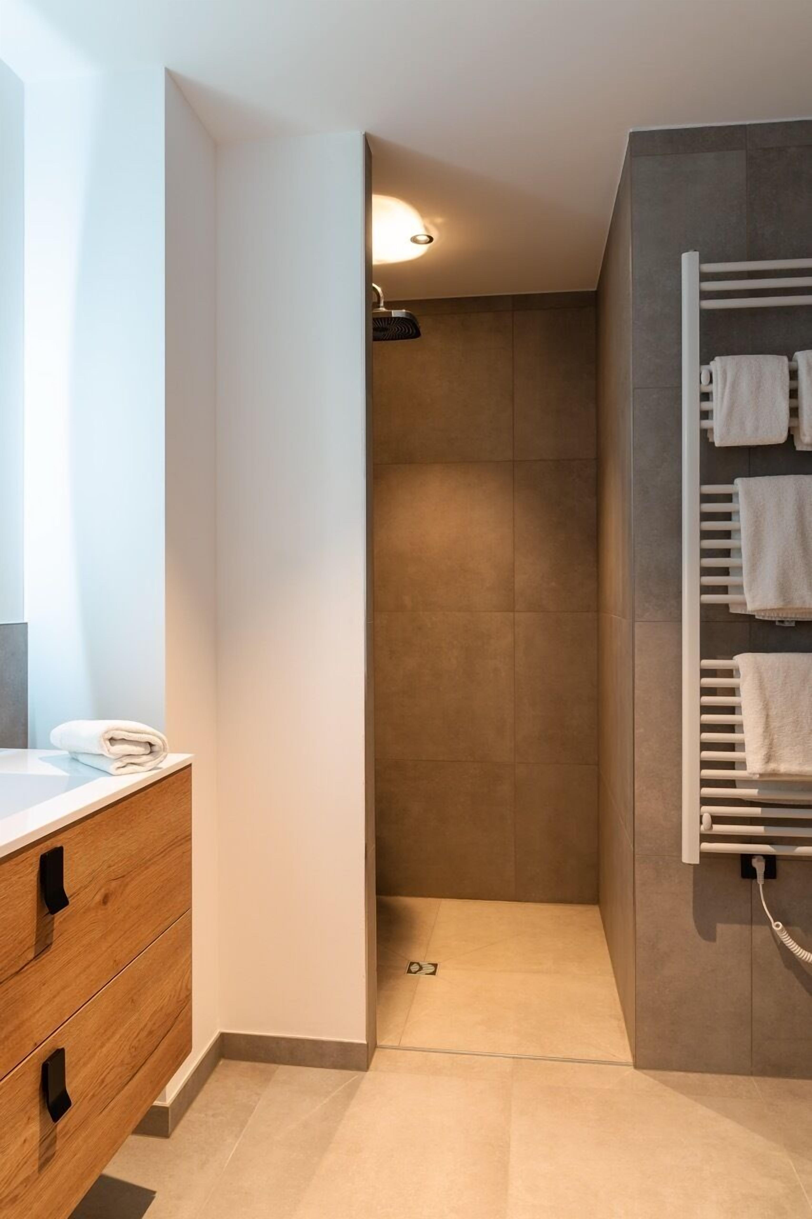 Ein modernes Badezimmer mit Dusche, Handtuchhalter und einem Holzkosmetikschrank mit Schubladen.