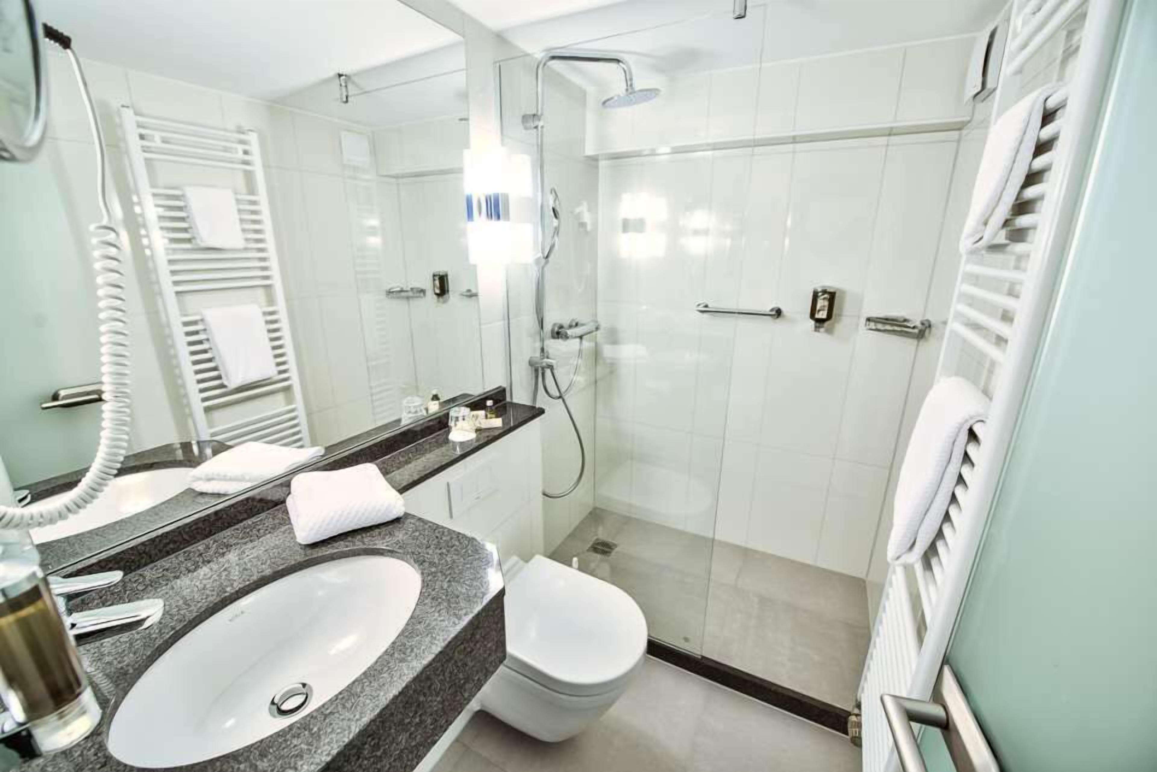 A modern bathroom with a granite countertop sink, a white toilet, a glass-enclosed shower, and a towel rack.