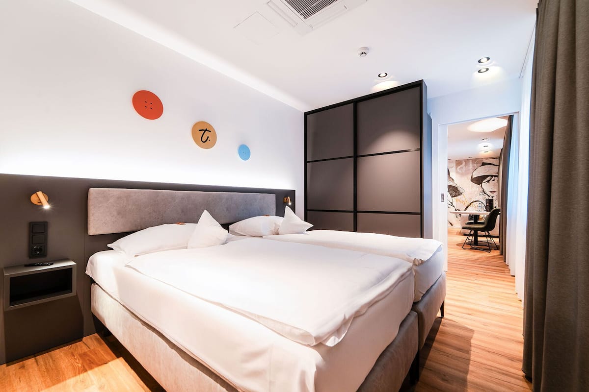 A modern hotel room with a large bed, a bedside table, and a wardrobe.