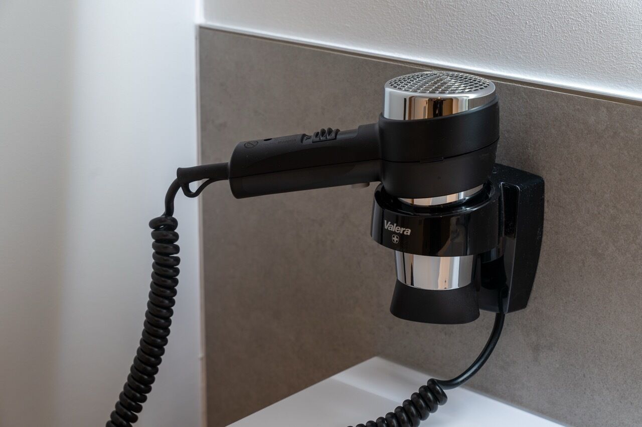 A hair dryer mounted on a wall with a cord.