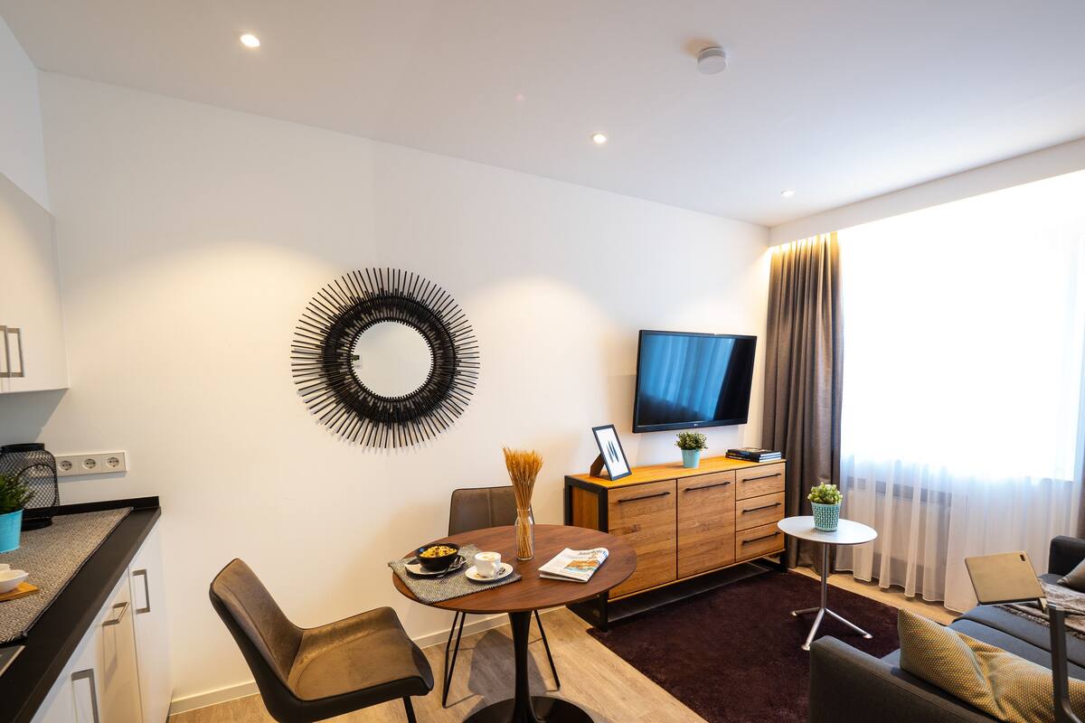 A modern living room with a round wall decoration, a flat-screen TV, a dining area with a table and chairs, and a sofa with a coffee table.