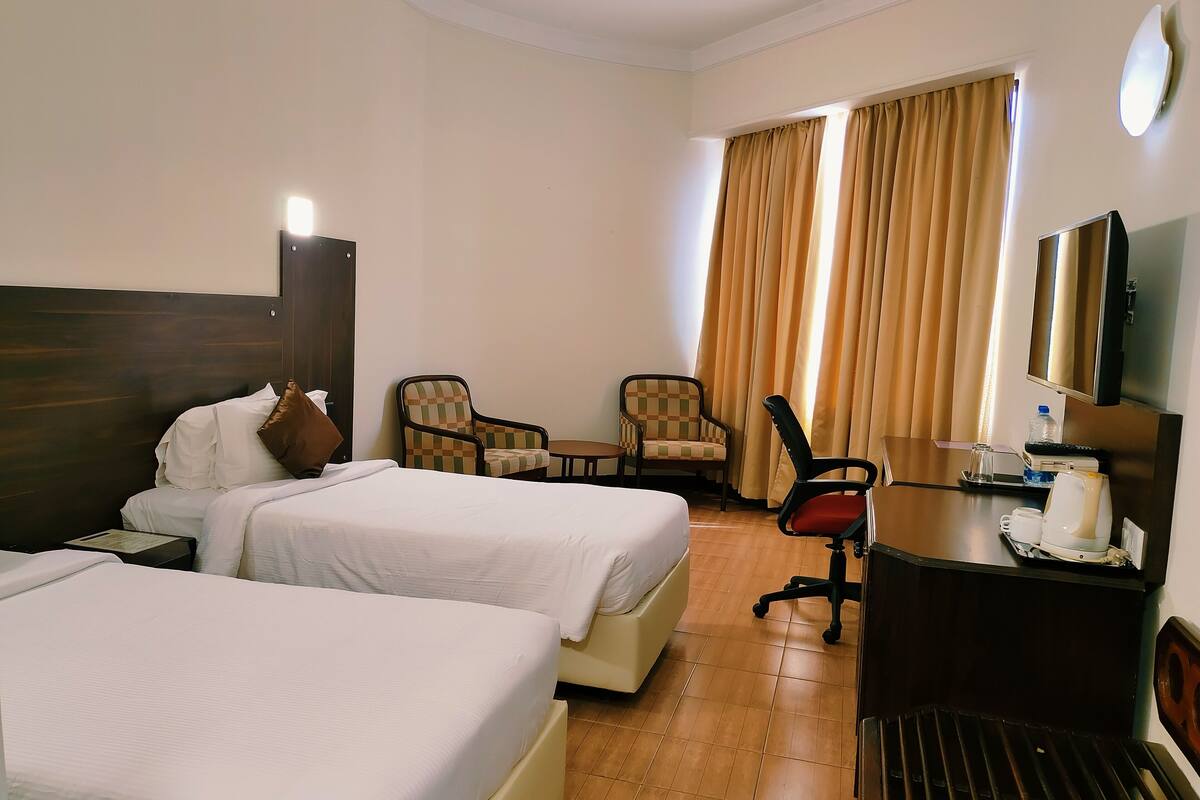 Habitación de hotel con dos camas, un escritorio con una computadora, una silla y un televisor.