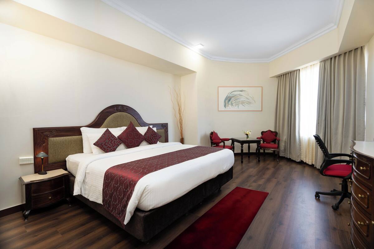 Habitación de hotel con una cama grande, un escritorio, dos sillas, un aparador y un cuadro en la pared.