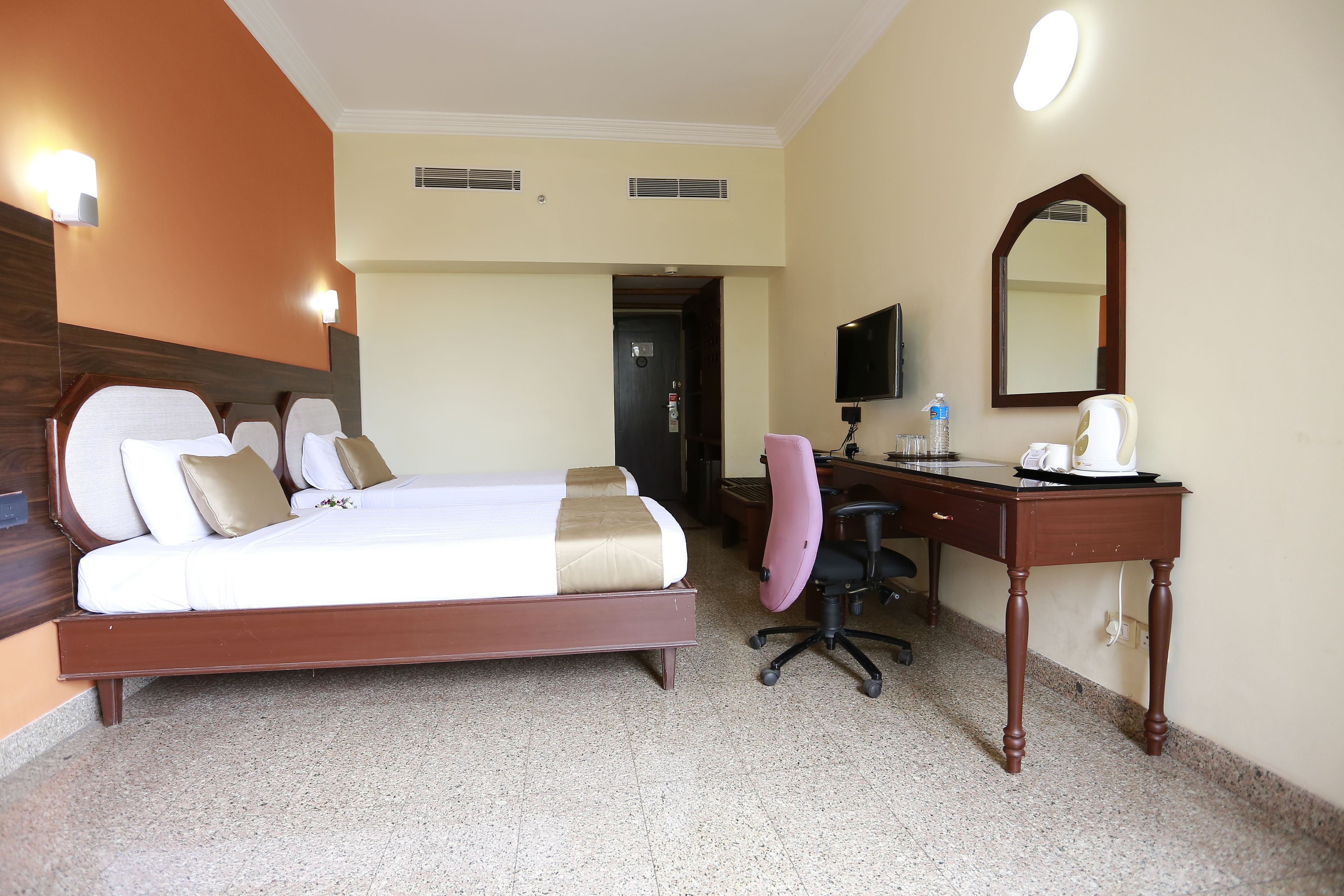 A hotel room with a bed, a desk, a chair, a mirror, and a television.