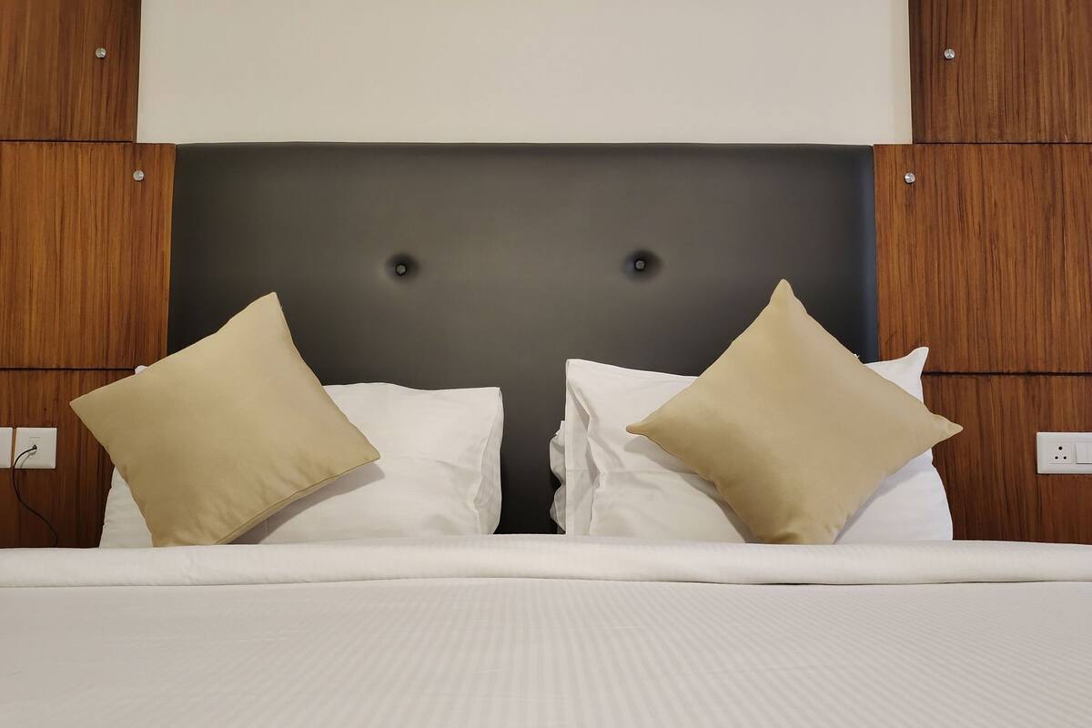 Habitación de hotel con una cama, dos almohadas color beige, un cabecero oscuro y paneles de madera en las paredes.