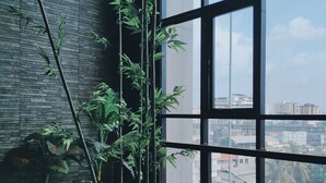 Une pièce dotée d’une grande fenêtre, de plantes en bambou et d’un mur en briques.