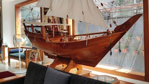 Une maquette de bateau est exposée dans une pièce dotée d’un plafond en bois, de grandes fenêtres et d’un canapé.