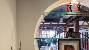 Une fenêtre circulaire donnant sur un coin repas, une œuvre d’art encadrée et une plante décorative.