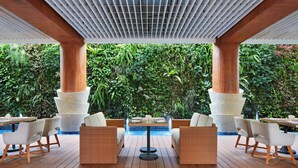 A covered outdoor seating area with wooden flooring, white cushioned chairs, and a central table. - Courtyard by Marriott Bandung Dago (Bandung)