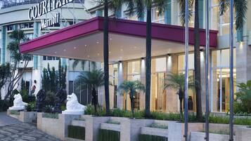 Entrada de un hotel Courtyard Marriott con un patio cubierto, palmeras y un camino empedrado.