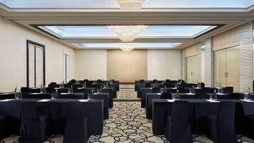 A conference room with a high ceiling, skylights, and a chandelier. Tables are arranged for meetings, with chairs and water bottles.