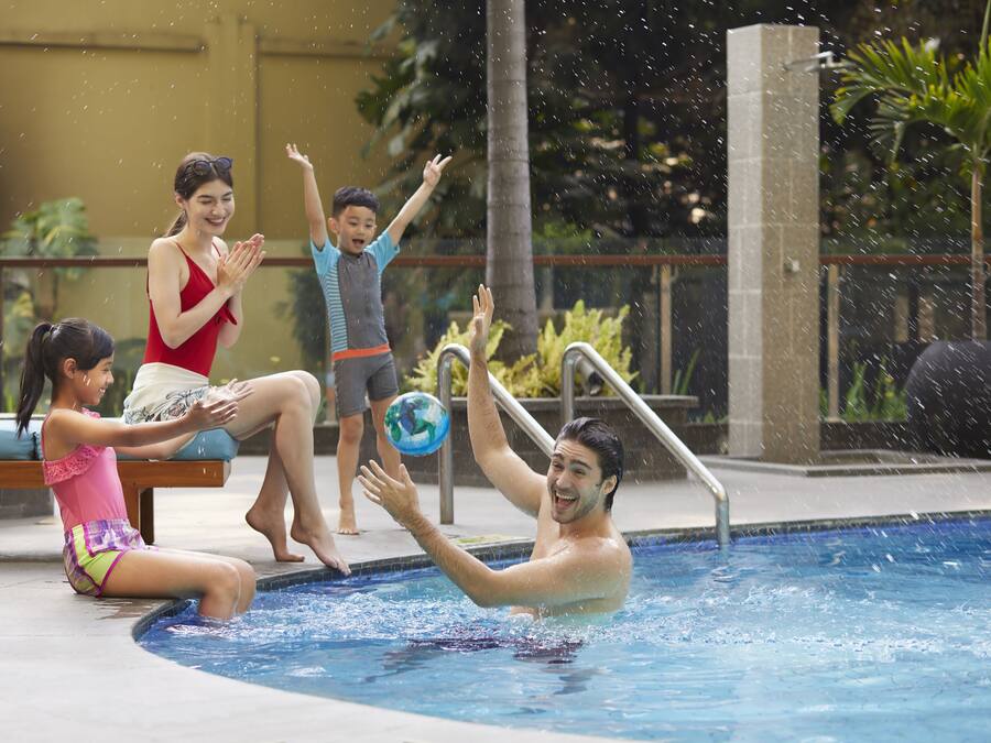 A swimming pool area with a water feature, a poolside seating area, and a view of the surrounding greenery.