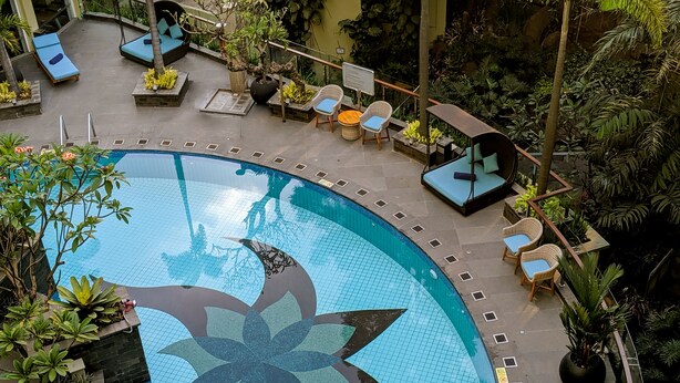 A pool with a geometric tile design, surrounded by lounge chairs and potted plants. - Courtyard by Marriott Bandung Dago (Bandung)