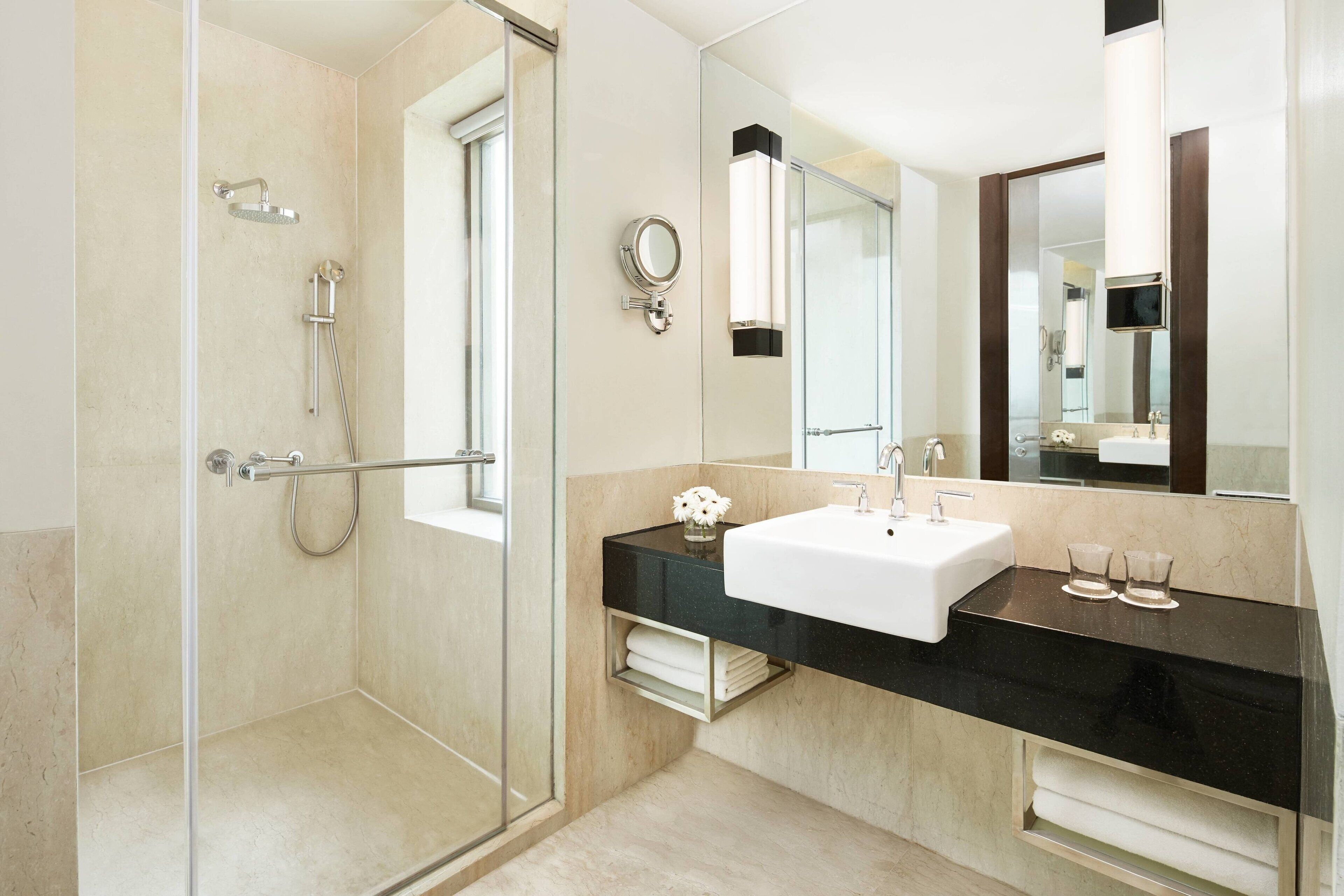 Un bagno moderno con doccia vetrata, un piano d'appoggio nero, un lavabo bianco e uno specchio grande.