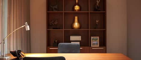Una sala de conferencias con una mesa de madera, dos sillas, una lámpara de escritorio, un teléfono y una estantería decorativa con diversos objetos.