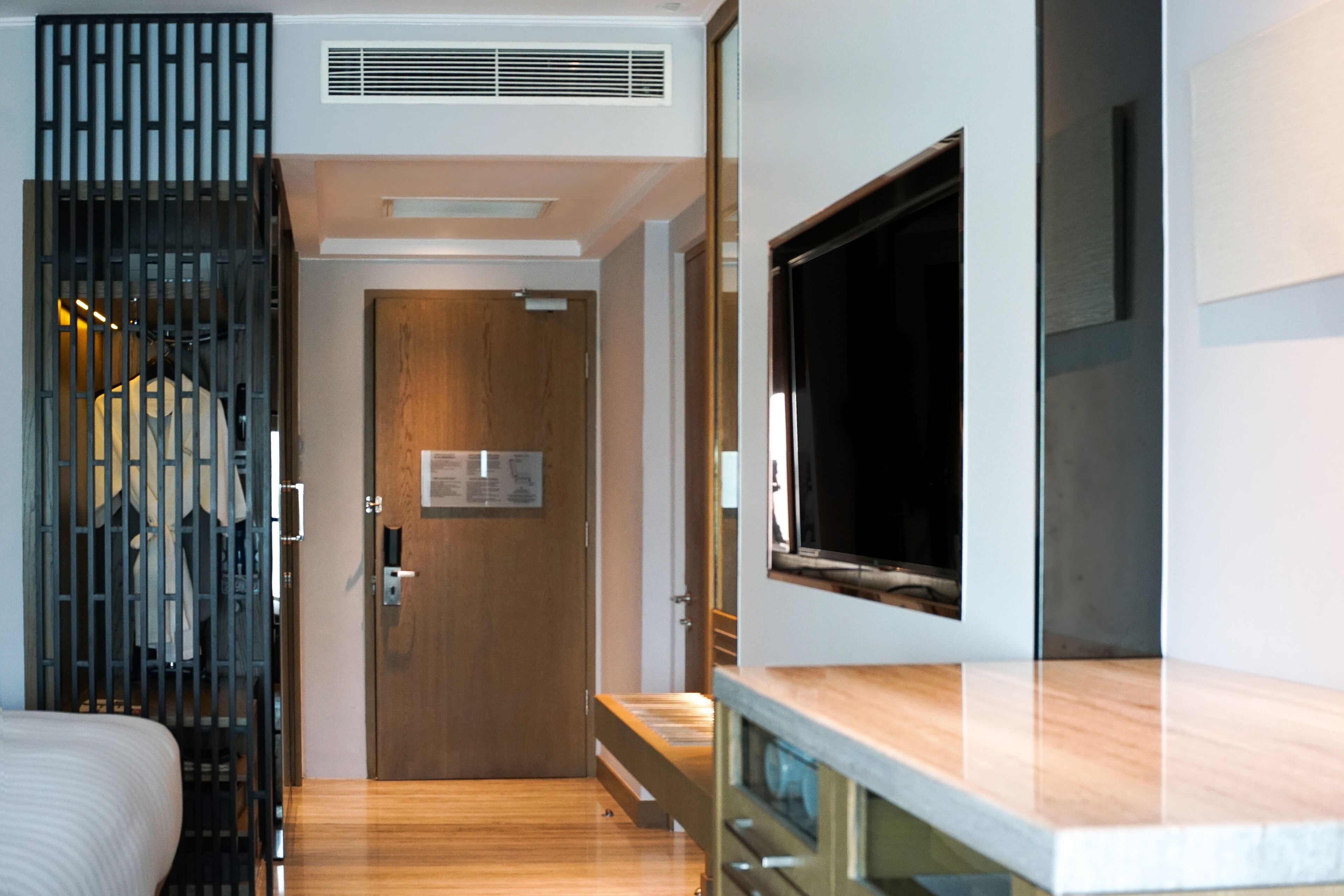 Habitación de hotel moderna con suelo de madera, una cama, un armario y un televisor fijado a la pared.