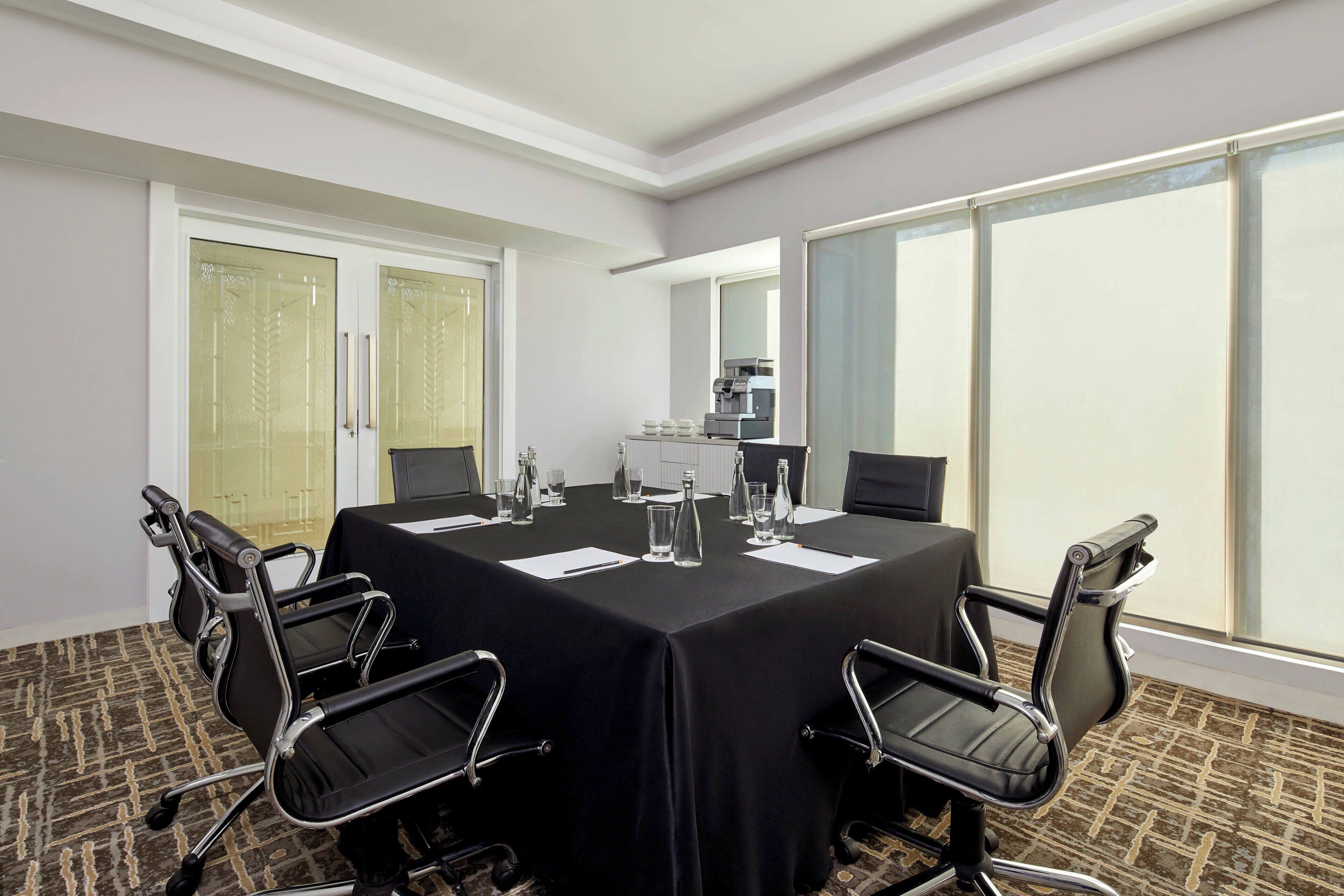 A conference room with a large table, black chairs, and a coffee machine.