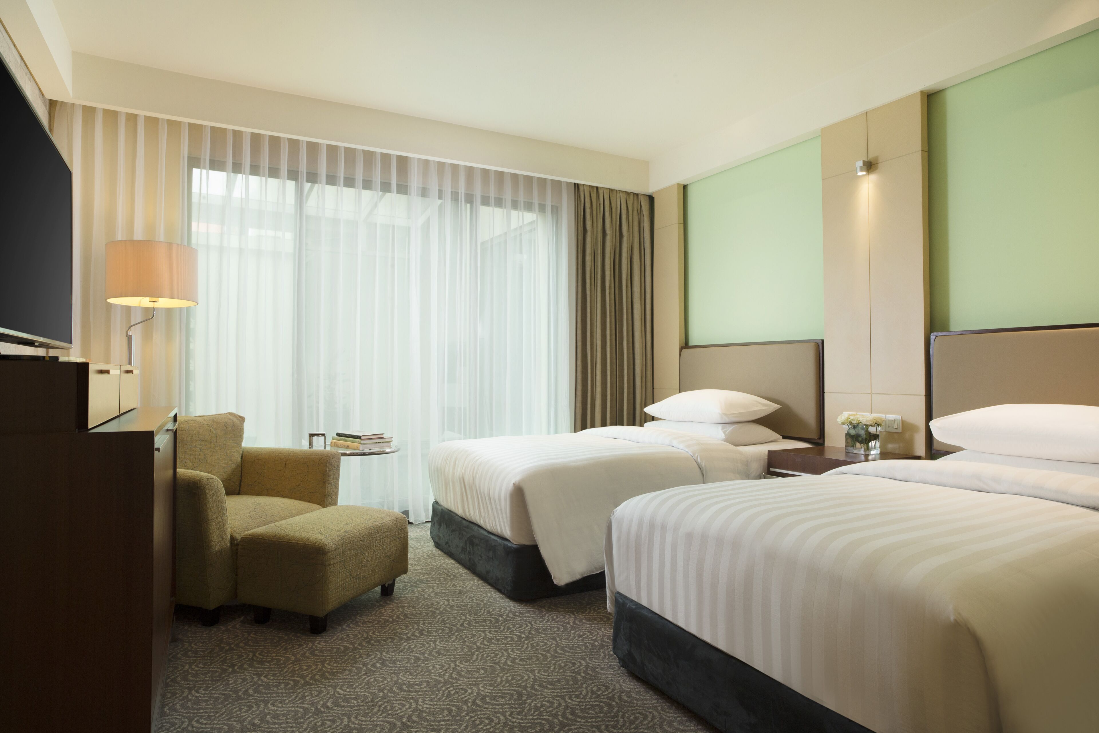 Une chambre d’hôtel avec deux lits, une chaise, une télévision et une fenêtre avec des rideaux.