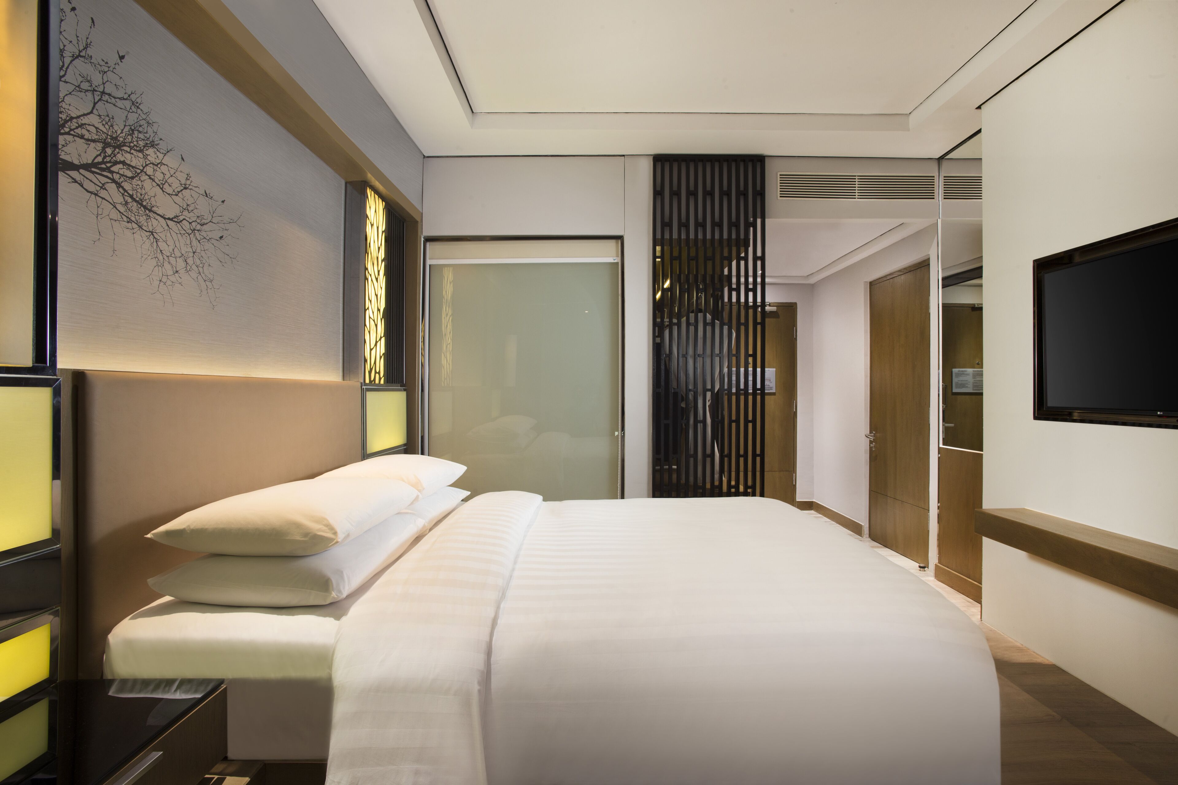 Una habitación de hotel moderna con una cama grande, una mesita de noche, un televisor de pantalla plana en la pared y una puerta corredera que da a un baño.