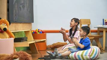 A child playing with toys in a room with a television, a wooden desk, and colorful balls.