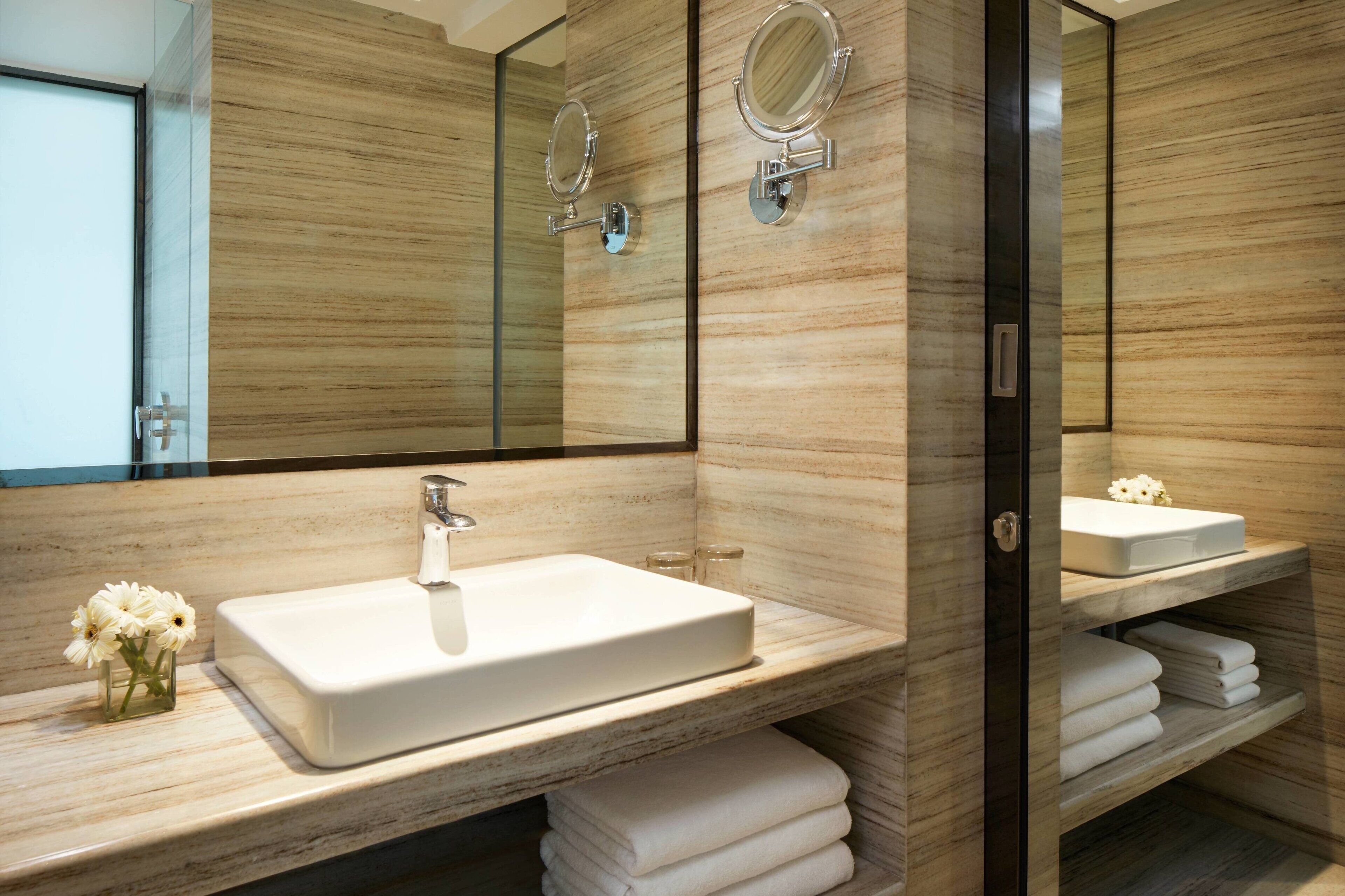 A modern bathroom with a large mirror, a white sink, and a vanity with towels.