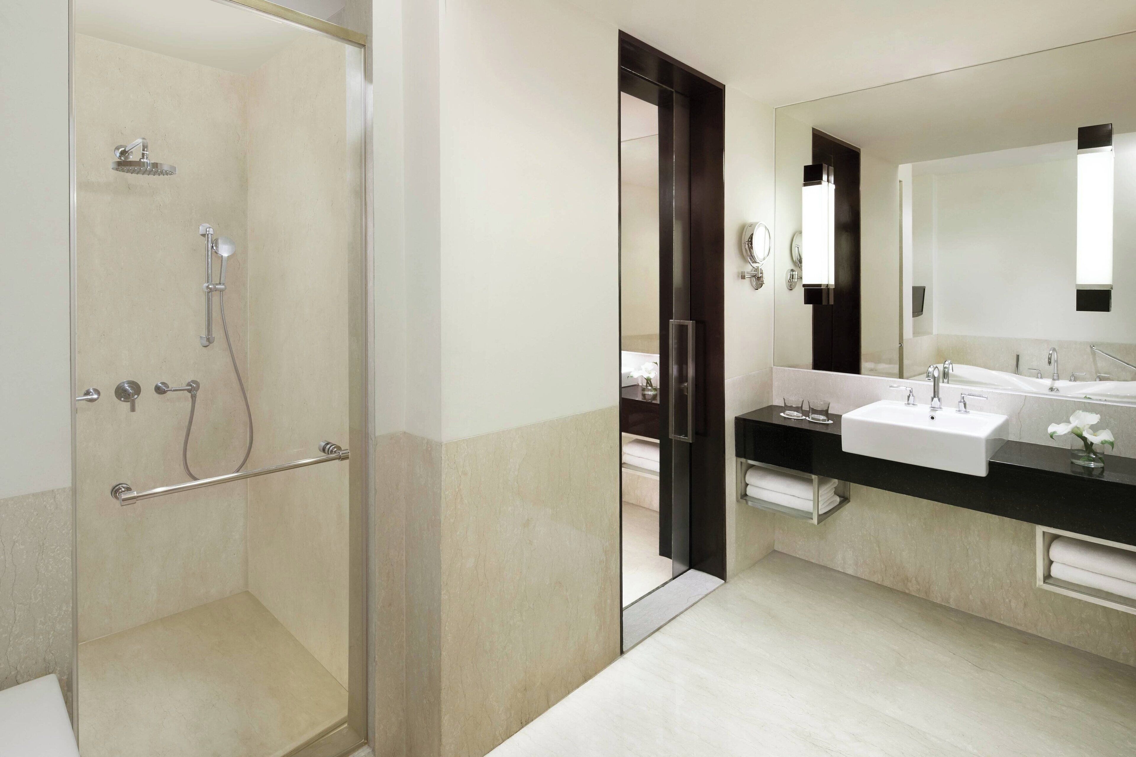 Une salle de bain moderne avec une douche à parois de verre, un grand miroir et un plan de toilette noir avec un lavabo blanc.