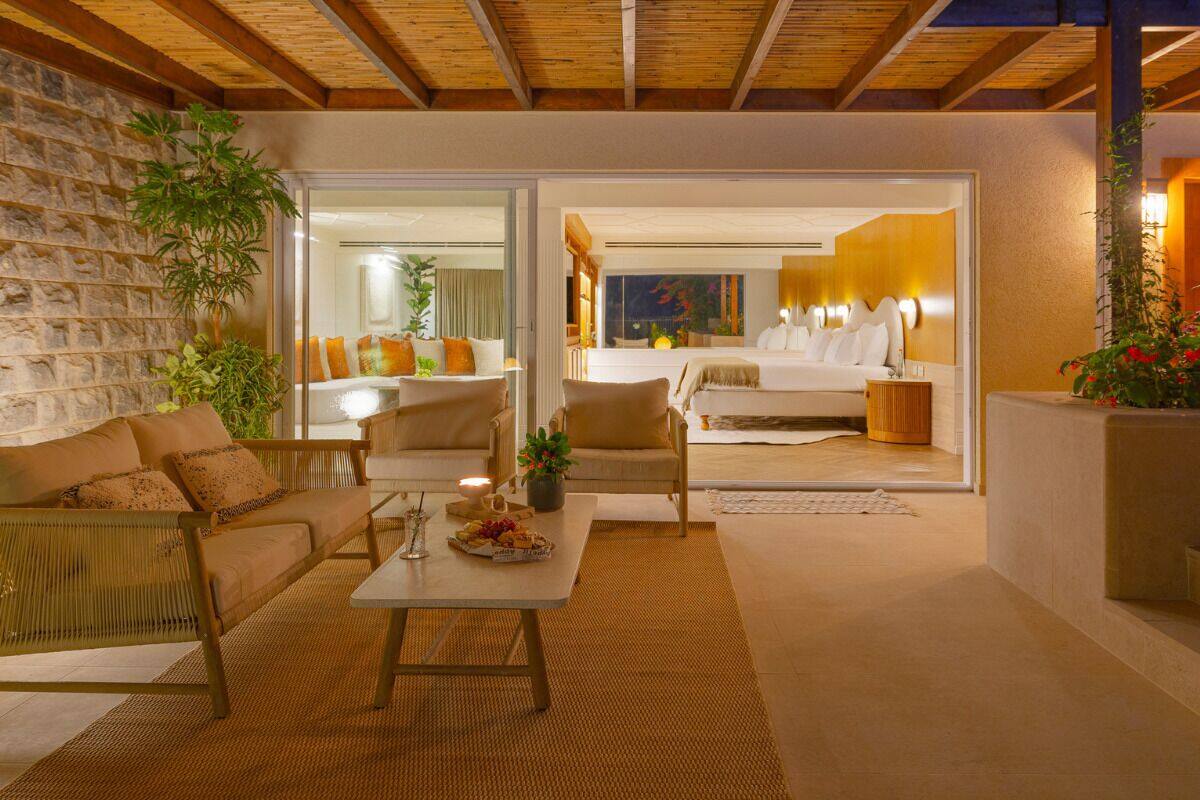 A cozy, well-lit room with a sofa, armchairs, and a coffee table. There is a large window with a view of the outside.