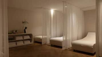 Two single beds with white bedding, a shelf with towels, and sheer curtains create a serene retreat.