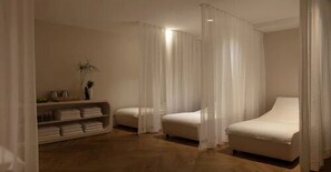 A bedroom with two beds, a shelf with folded towels, and sheer curtains.