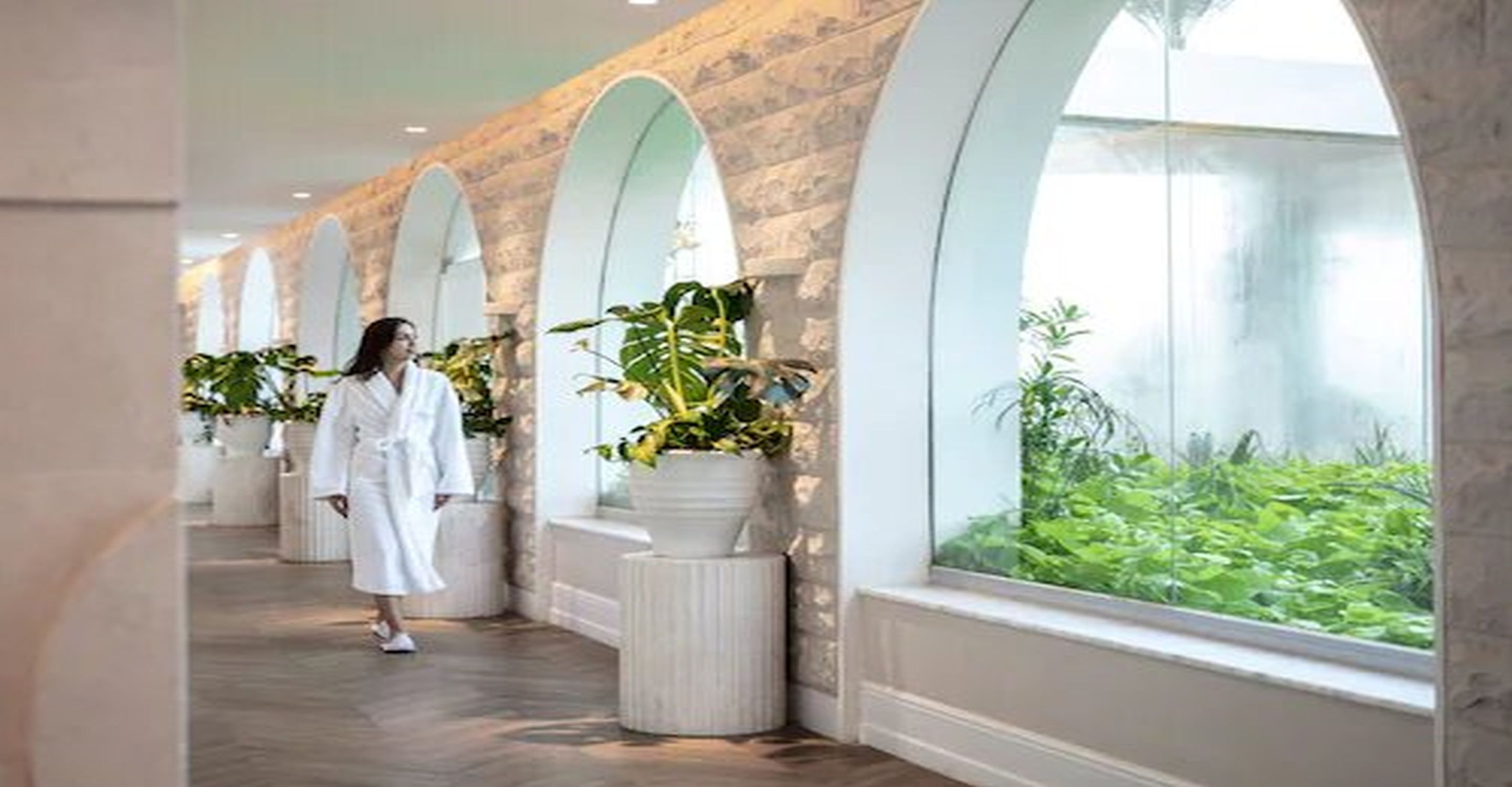 A corridor with arched ceilings and large windows overlooking a lush green garden.