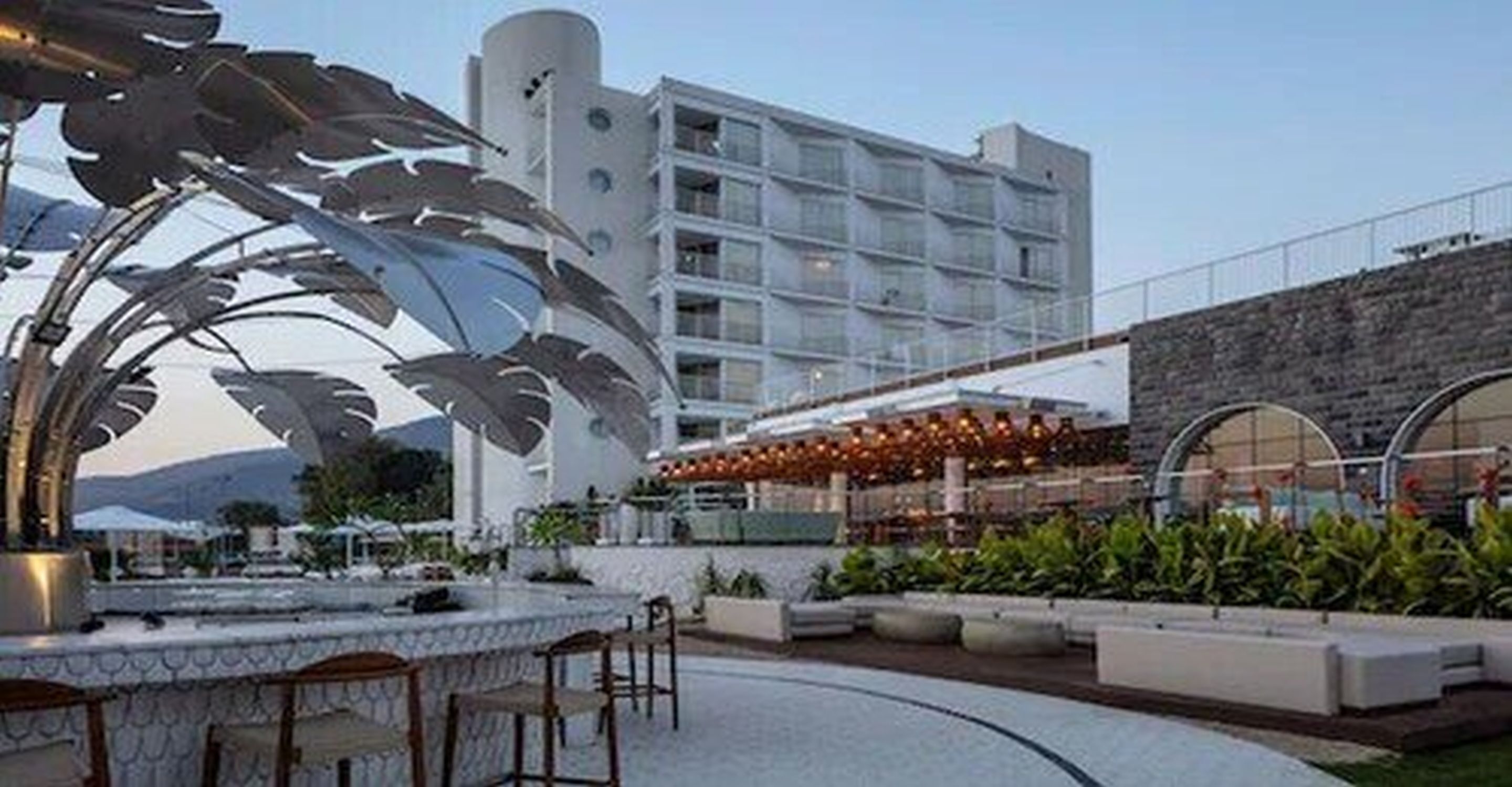 Un hotel moderno con bar en la azotea, mesas al aire libre y una gran escultura decorativa de metal.
