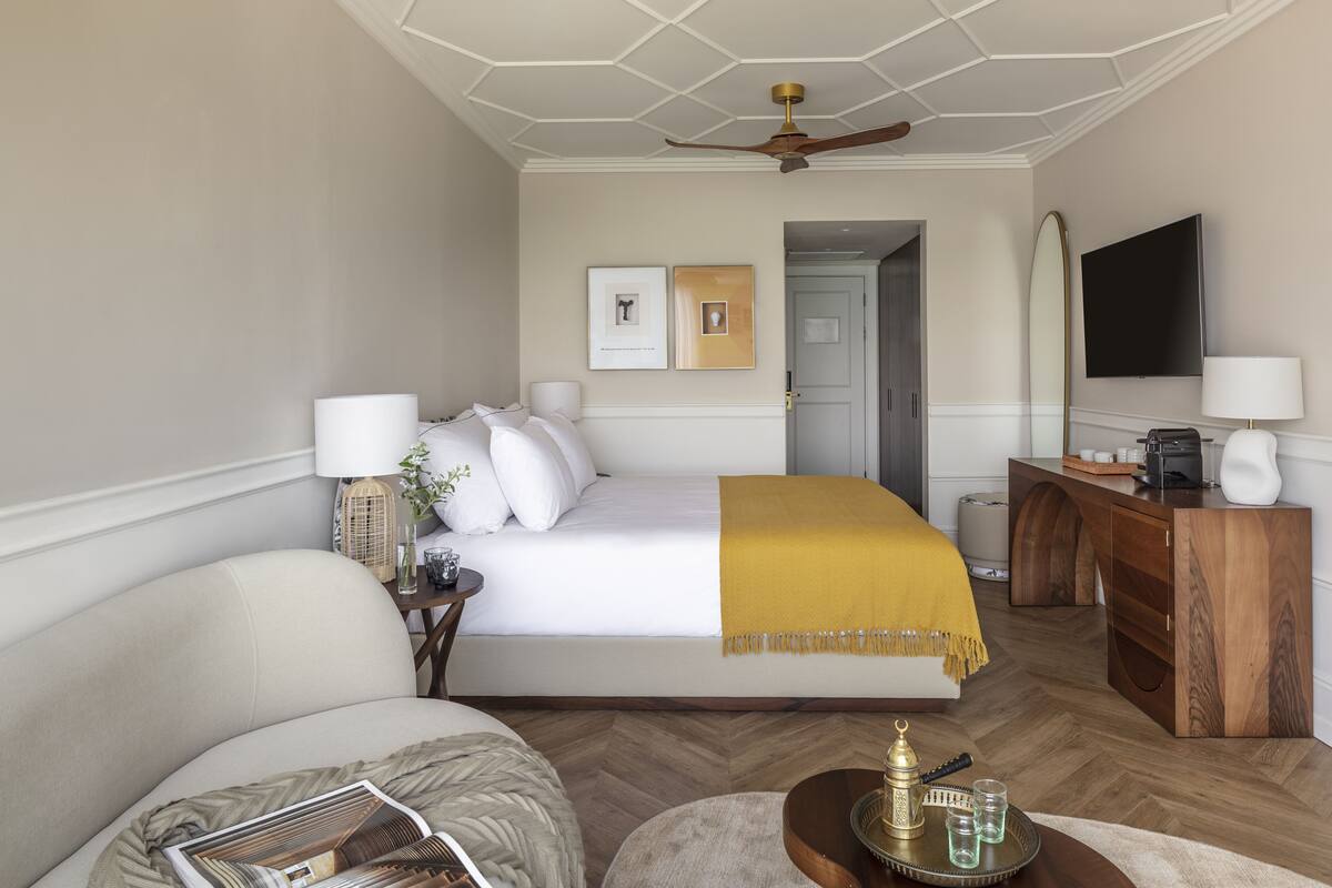 A hotel room with a bed, a desk, a chair, a television, and a ceiling fan.