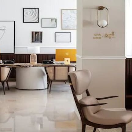 A modern office space with a long table, two chairs, and a laptop. There are framed artworks on the wall and a decorative wall piece.