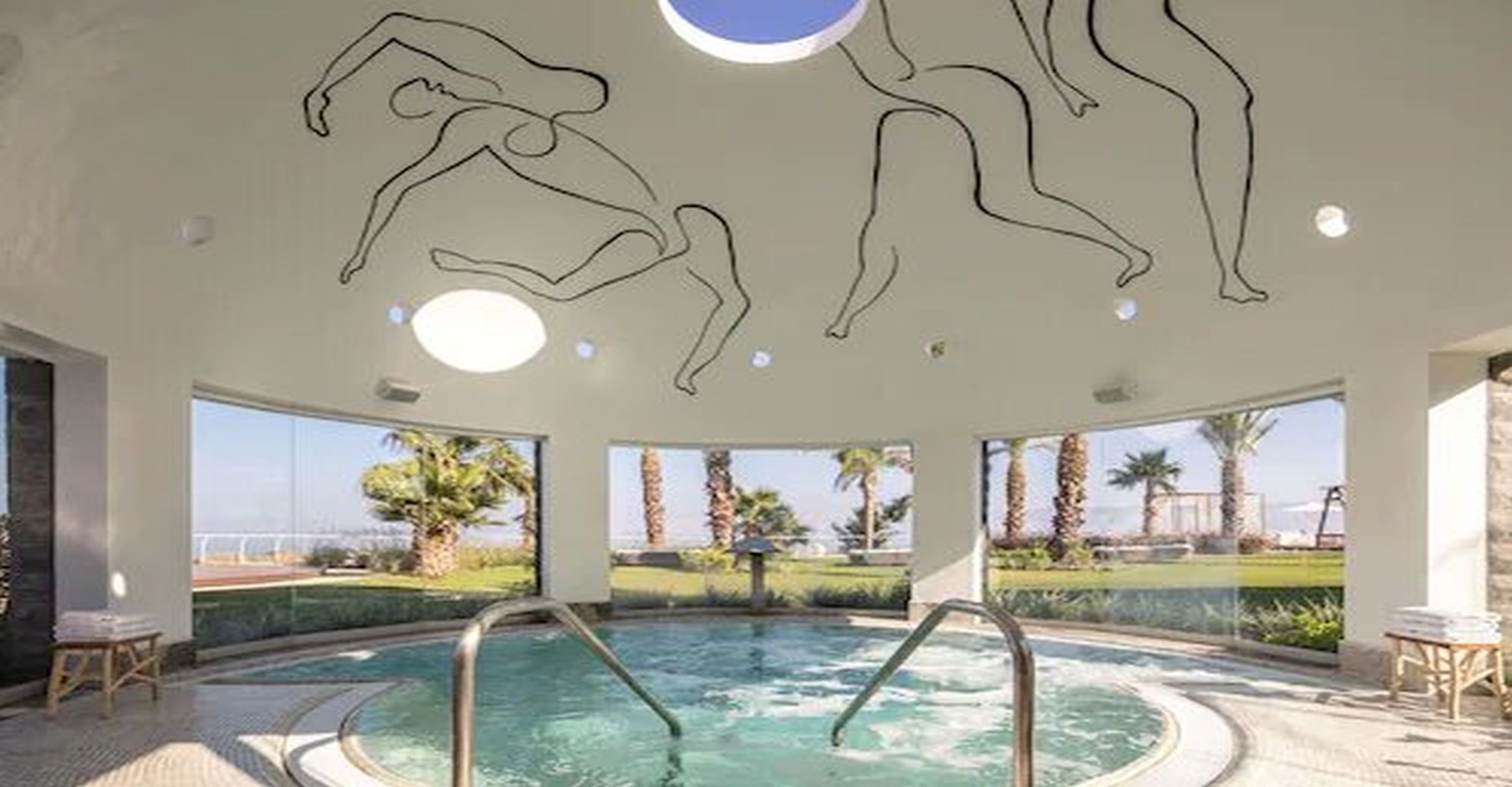 Uma área de piscina com hidromassagem, vista clara para palmeiras e paisagem distante, e teto com arte abstrata em linhas.