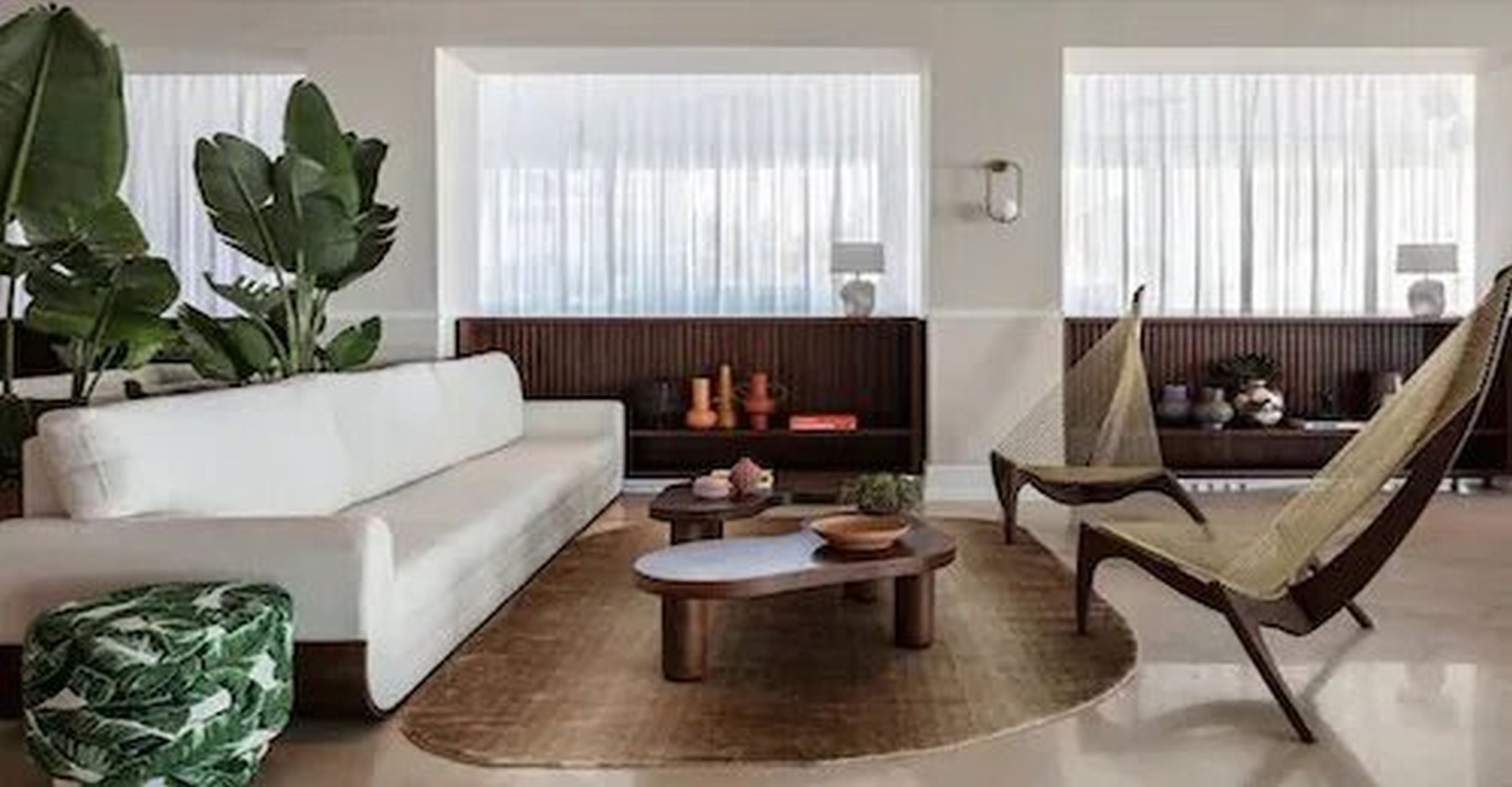 A living room with a white sofa, a wooden coffee table, a green patterned ottoman, and a wicker chair.