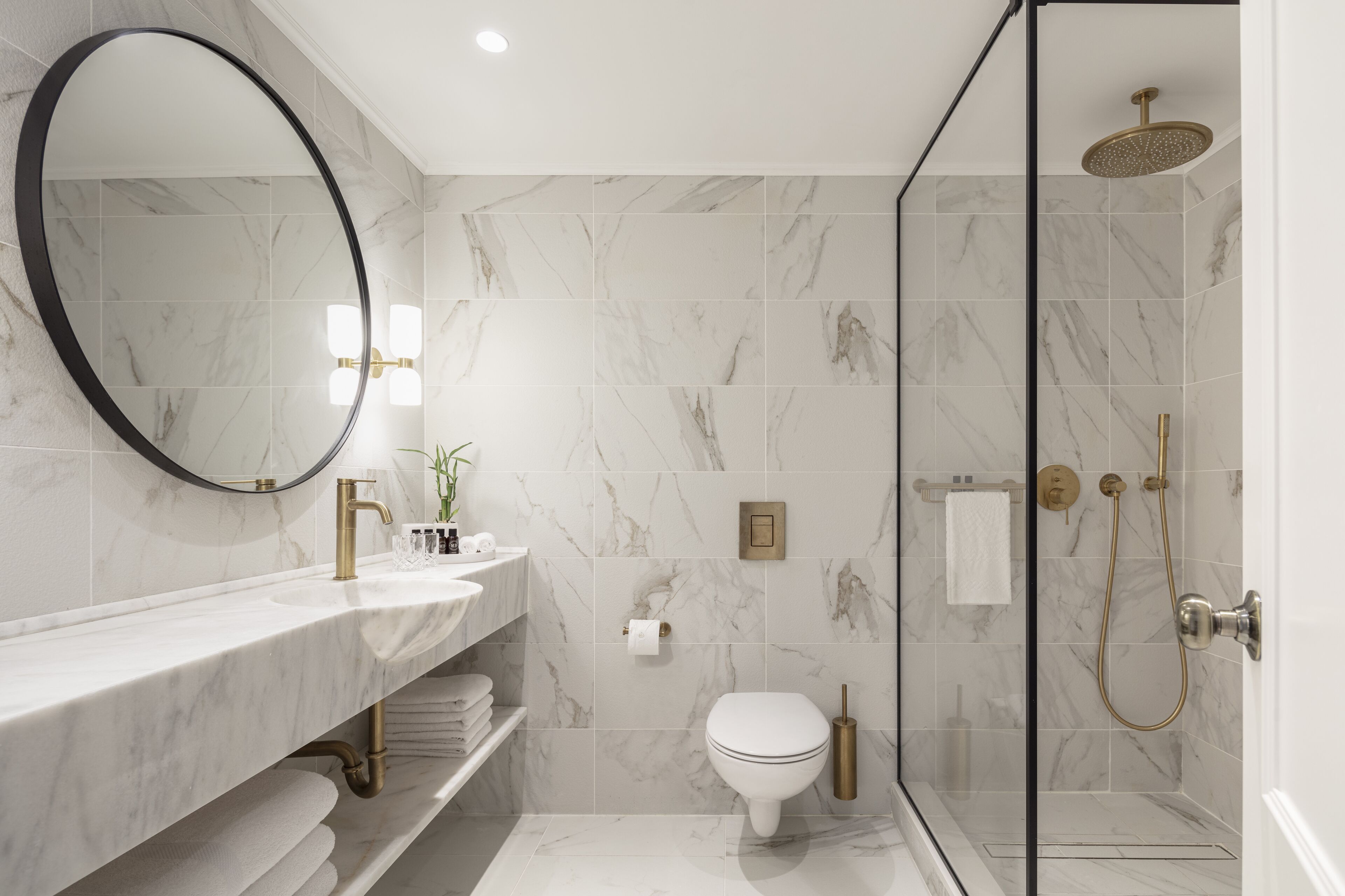 A modern bathroom with a marble sink, a toilet, and a glass-enclosed shower.