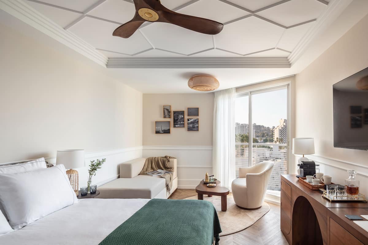 A hotel room with a bed, two seating areas, a coffee station, and a view of the city.