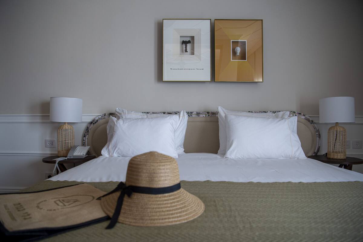 A hotel room with a bed, two bedside tables with lamps, a telephone, and two framed pictures on the wall.