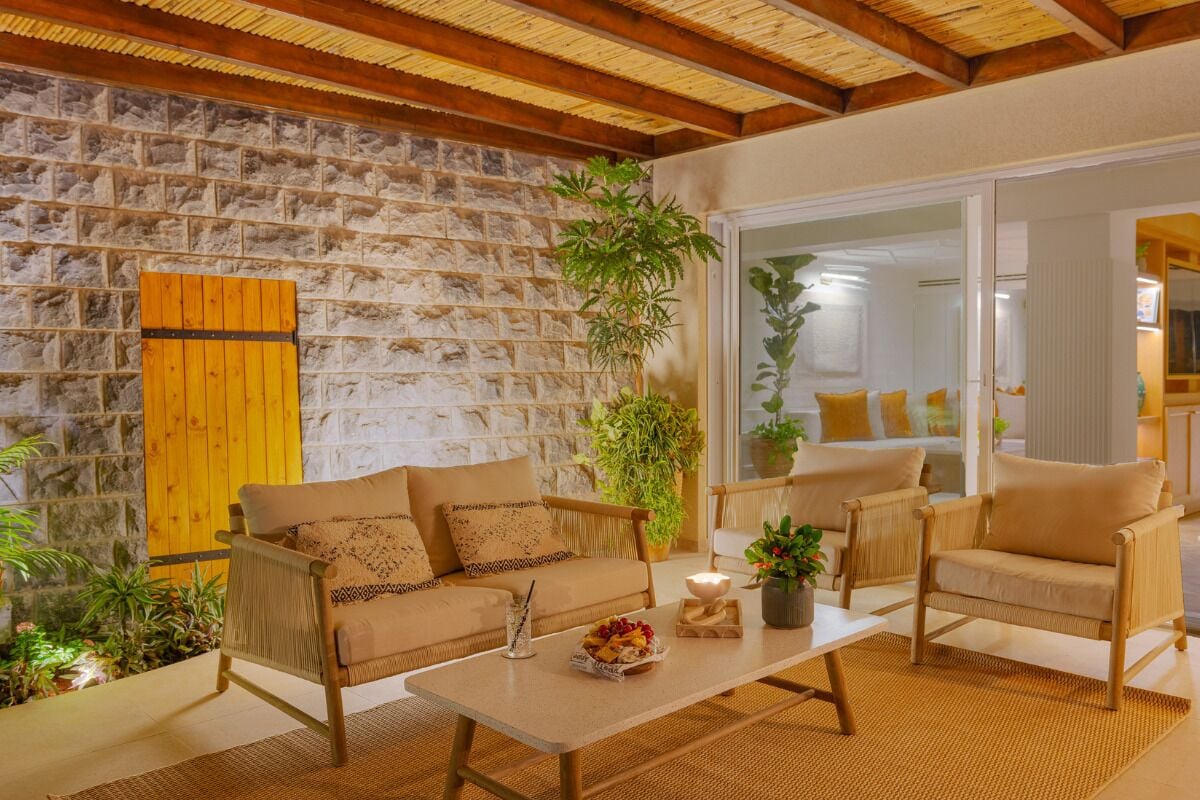 A cozy room with a stone wall, wooden ceiling, and a large window. There are two sofas and a coffee table with a plant and a candle.