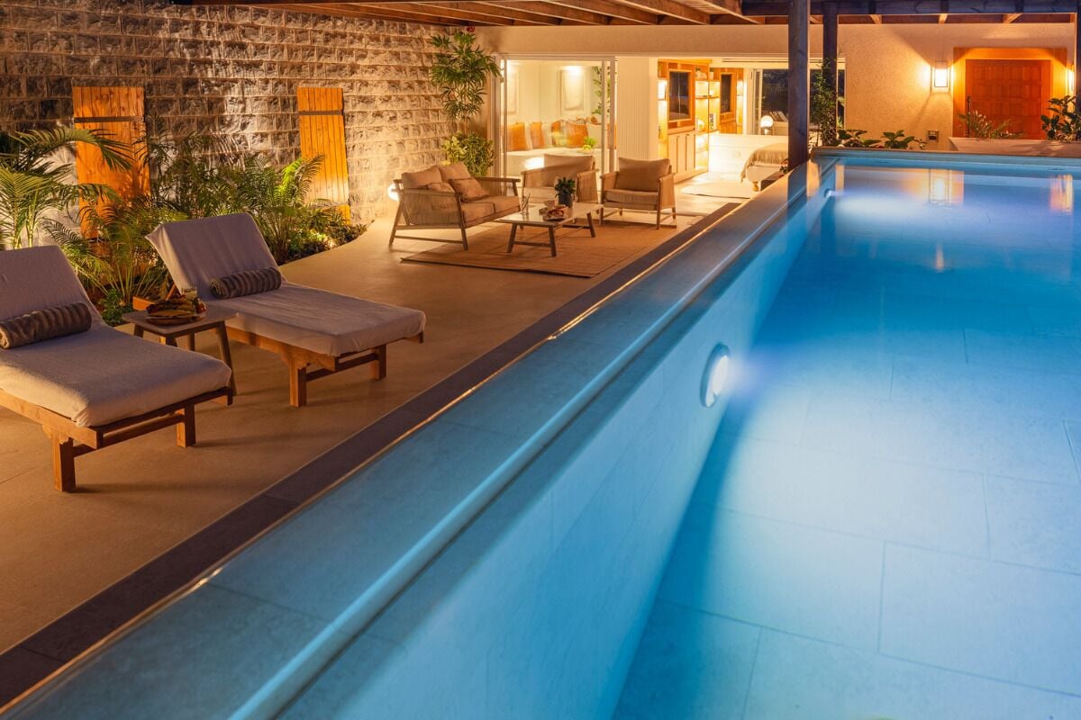 A poolside area with lounge chairs, a stone wall, and a well-lit interior.