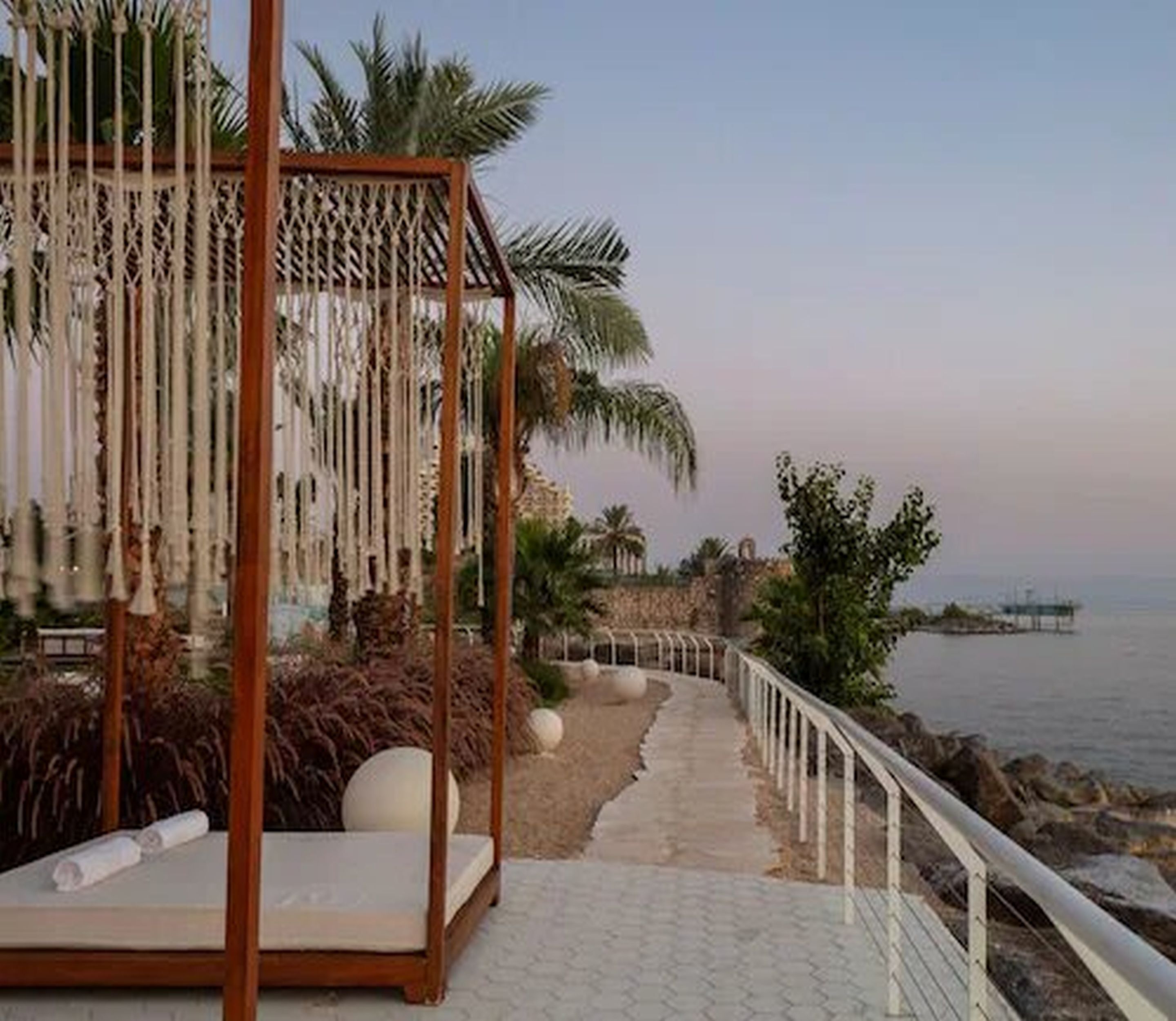 Un paseo marítimo en la playa con un columpio de madera, palmeras y vista al mar.