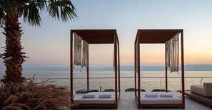 Two open-air beds with wooden frames and white cushions, overlooking a calm sea at sunset. - Galei Kinnereth Hotel (Tiberias)