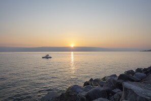 A calm sea at sunset with a boat and rocky shore.