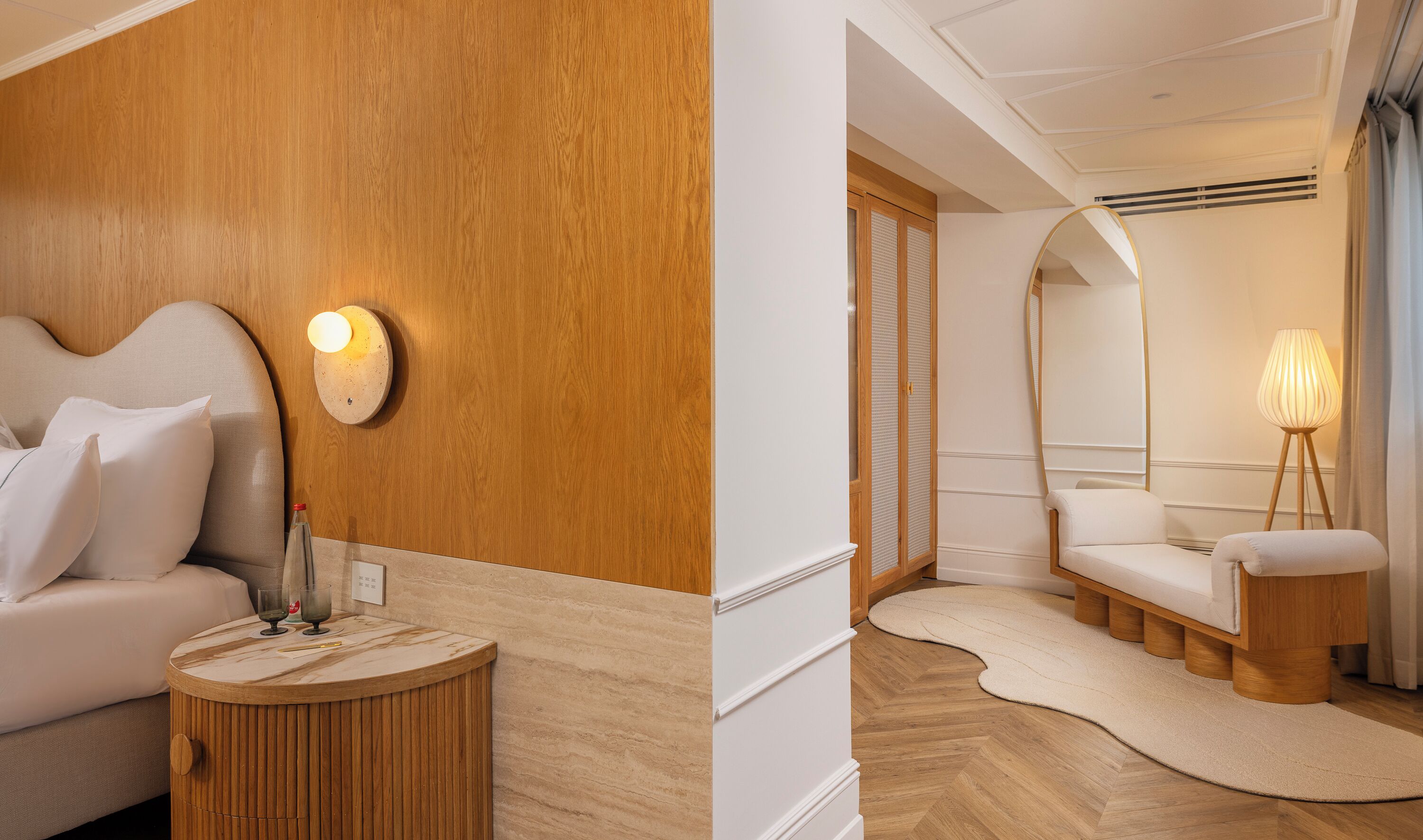Camera d'albergo con una parete in legno decorativa, un tavolino rotondo con un bicchiere e un letto con biancheria da letto bianca.